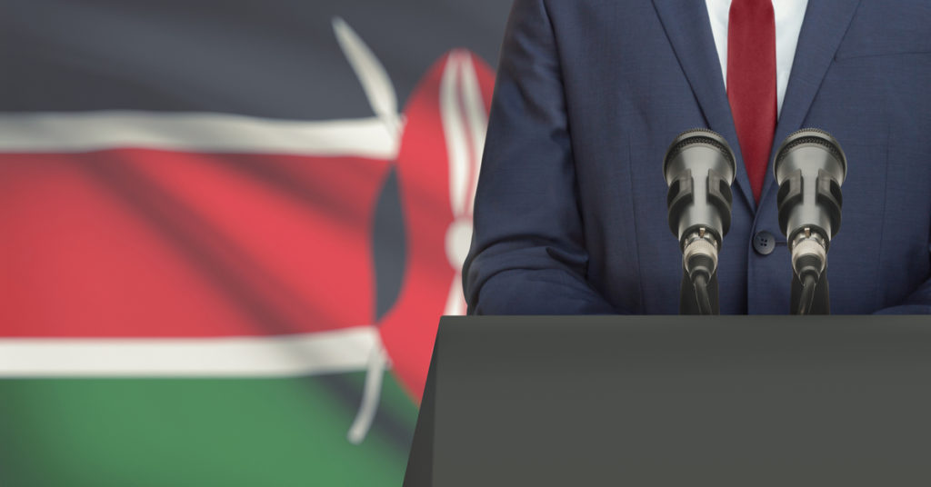 Speech podium with anonymous suited man, with Kenyan flag in background