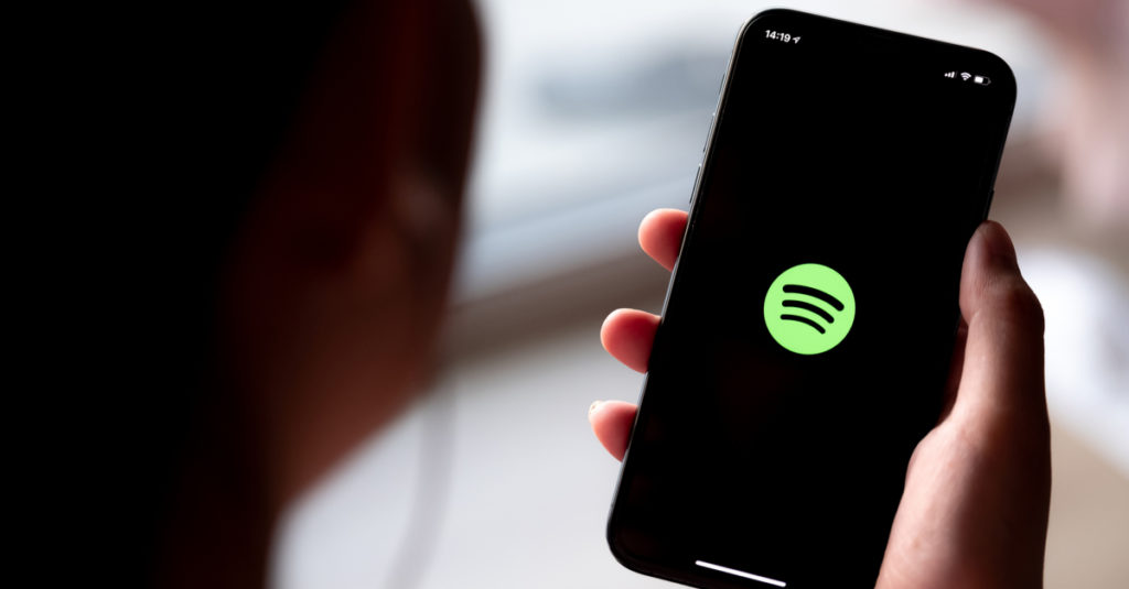 Smartphone displaying Spotify icon held by anonymous person.