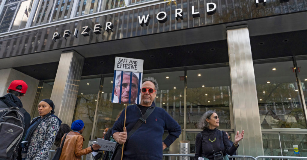 Protestor holding sign outside Pfizer building.