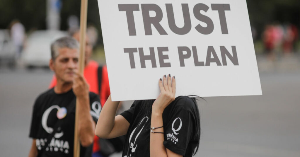 QAnon supporter holding sign saying "Trust the plan"