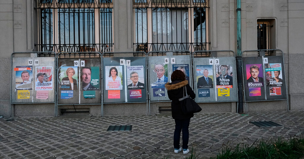 People walk in front of campaign posters on a board outside a polling station during the first round of France presidential elections at a polling station in Lille, France on April 10, 2022.