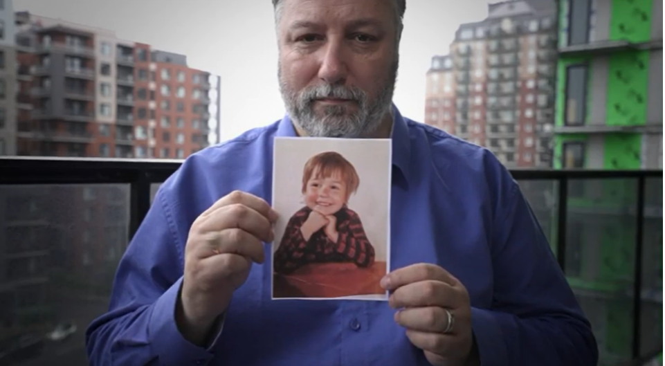 Sylvain, a former conspiracist, holds up a picture from his childhood. 